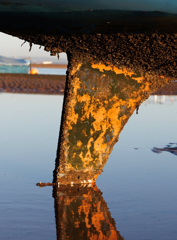 Rusty boat keel reflected in water at low tide, highlights nautical decay.