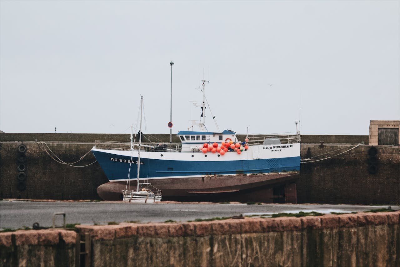 A fishing boat docked in a harbor with colorful buoys, against a calm sea backdrop.